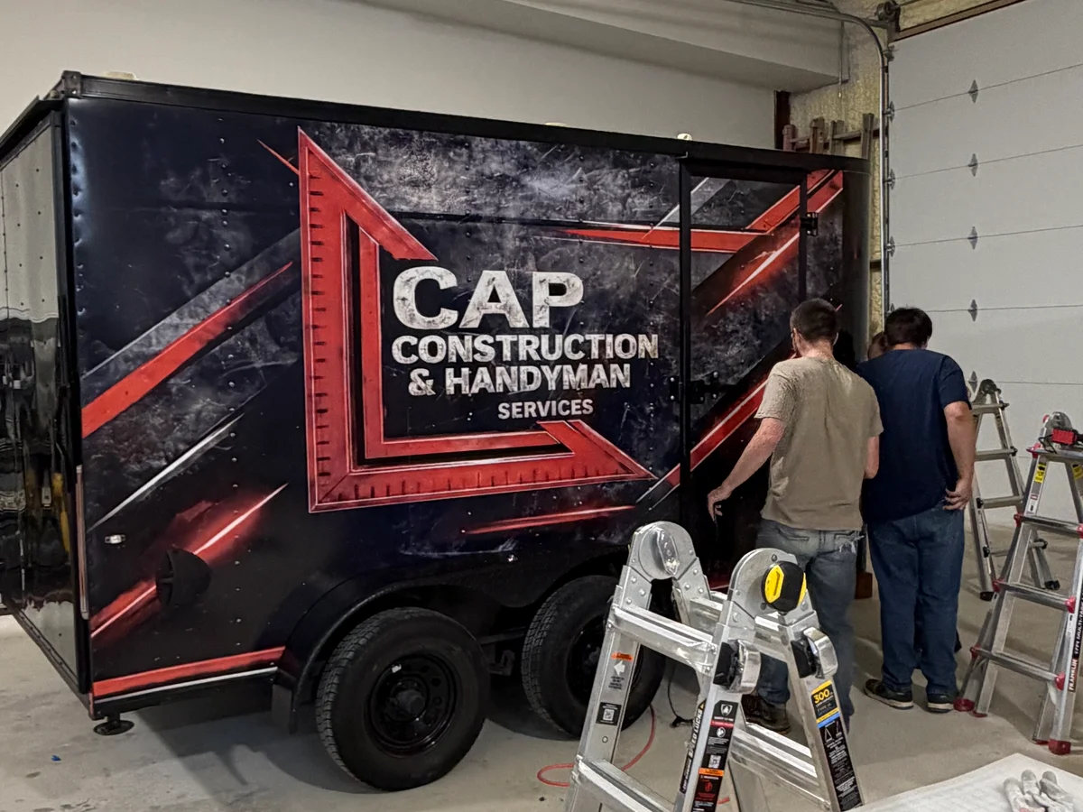 Workers installing CAP Construction trailer wrap